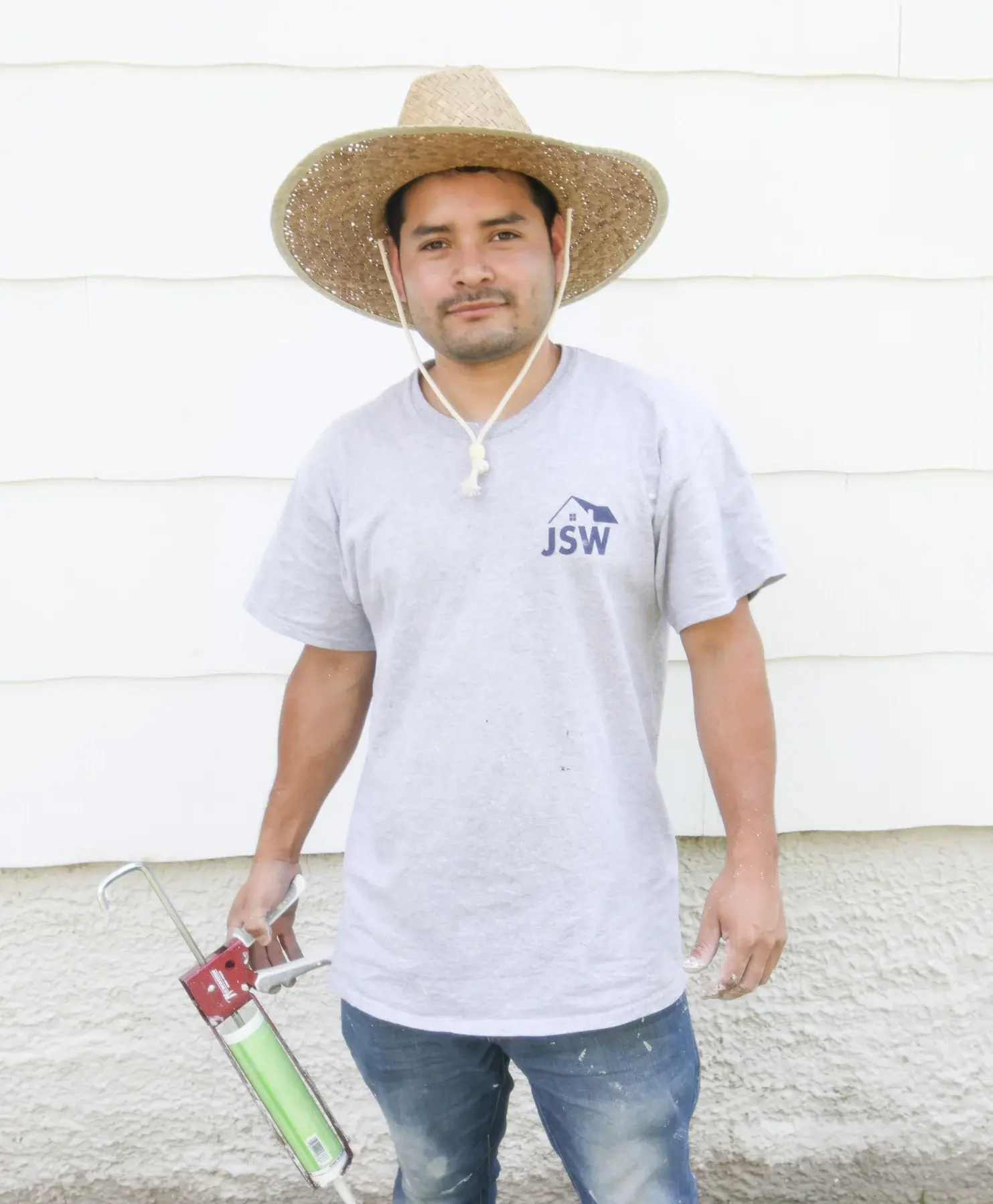 JSW crew member in a gray company shirt holding a tool at an exterior jobsite
