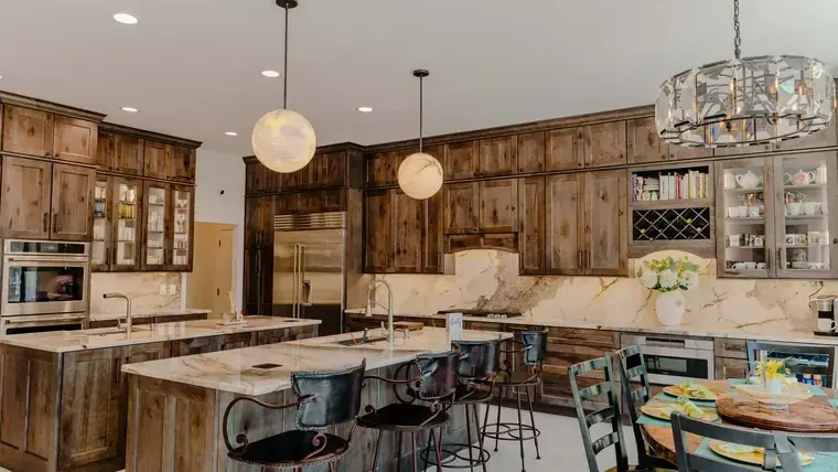 Finished natural-wood kitchen with two islands, stone counters, and layered pendant lighting