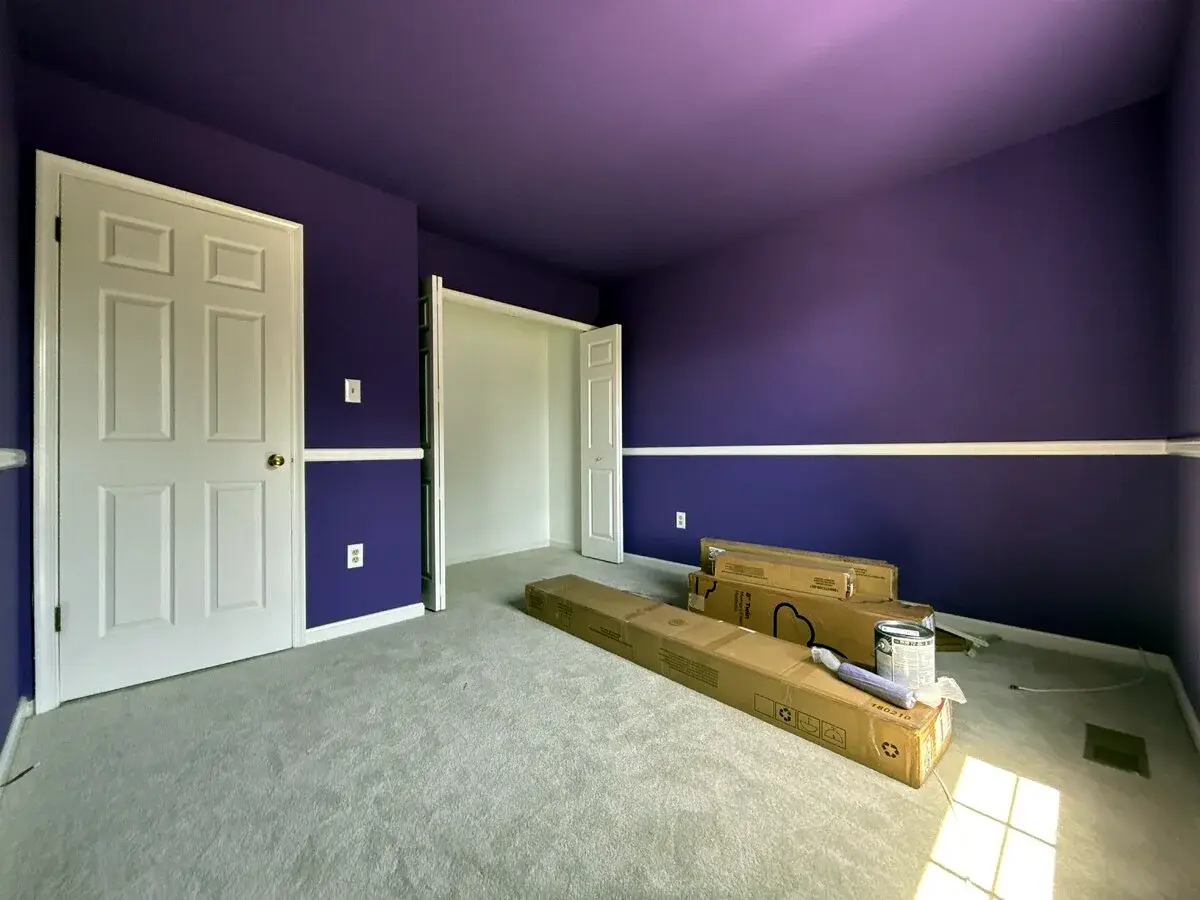 Wide view of a finished purple bedroom with white chair rail