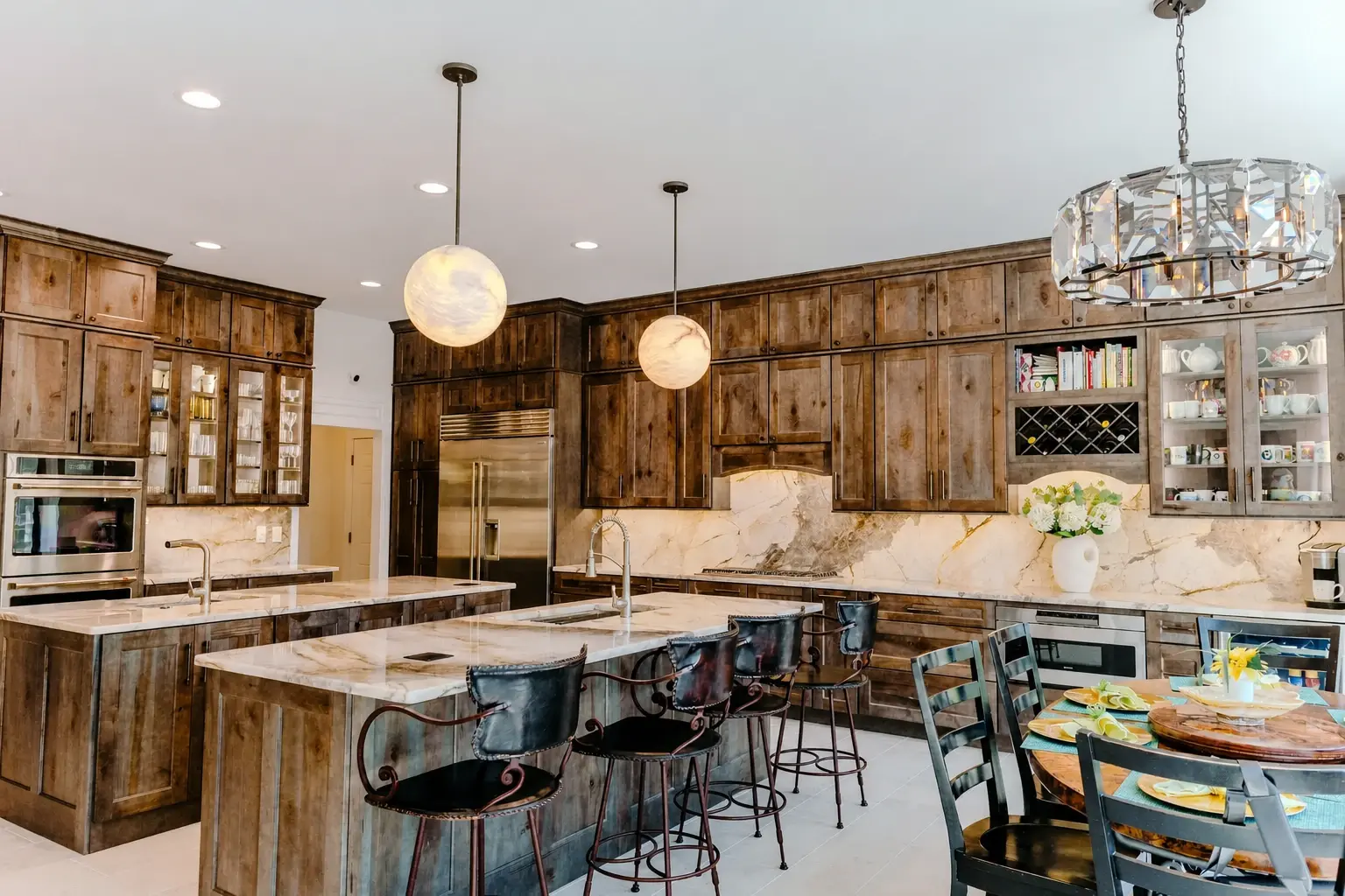 Finished warm wood kitchen with island seating, stone surfaces, and layered pendant lighting