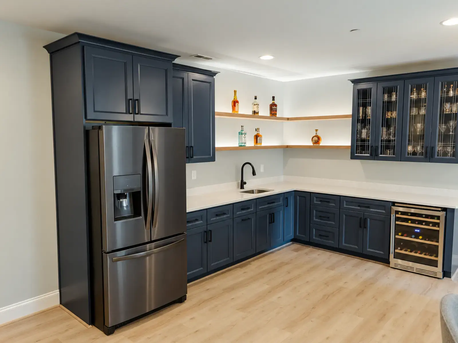 Finished basement wet bar with deep blue cabinetry, white counters, open shelves, and pale flooring