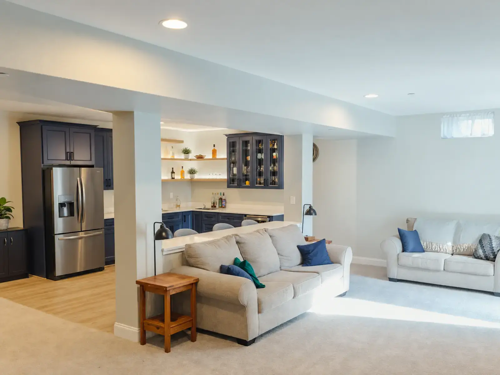 Finished basement lounge with seating, pale flooring, and an adjoining blue wet bar