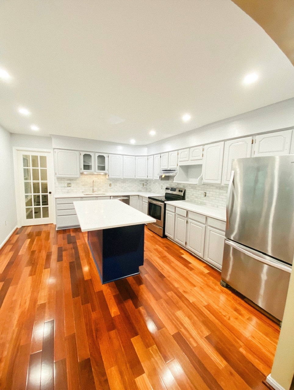 Finished kitchen with white perimeter cabinetry, a blue island, and coordinated counters and hardware