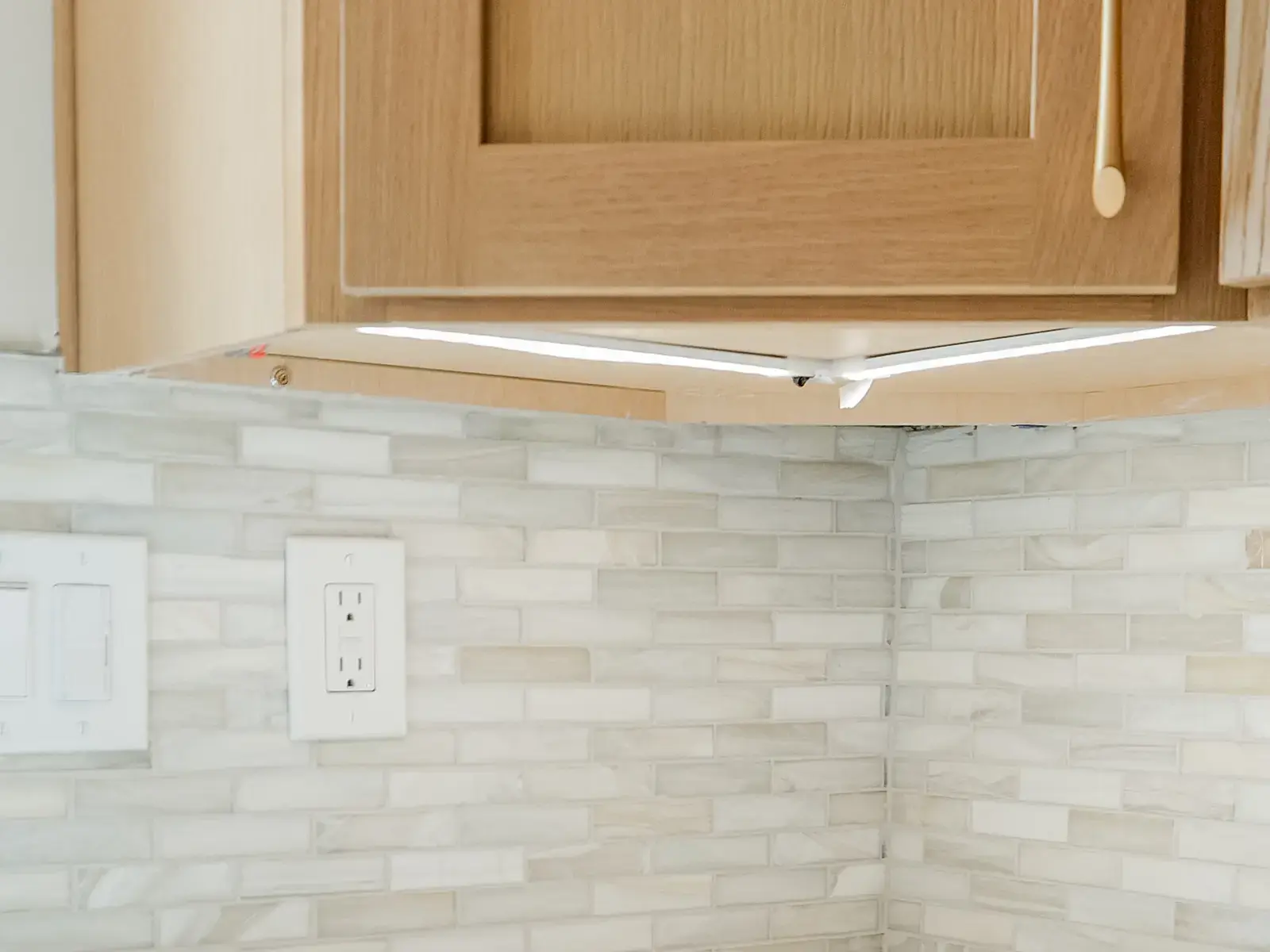 Close view of a finished light mosaic kitchen backsplash beneath warm wood cabinets