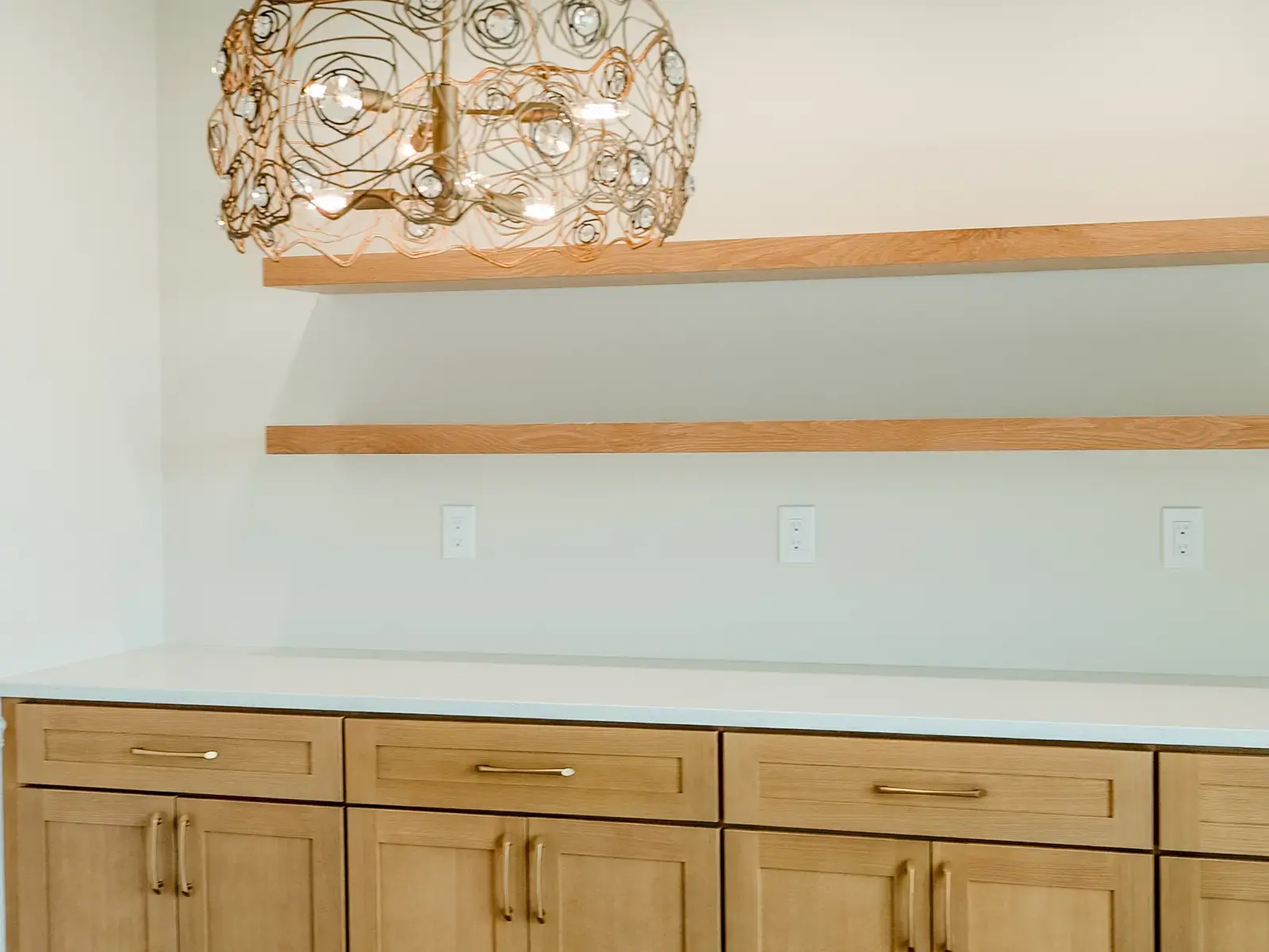 Finished kitchen beverage wall with wood cabinetry, open shelving, pale counters, and decorative tile