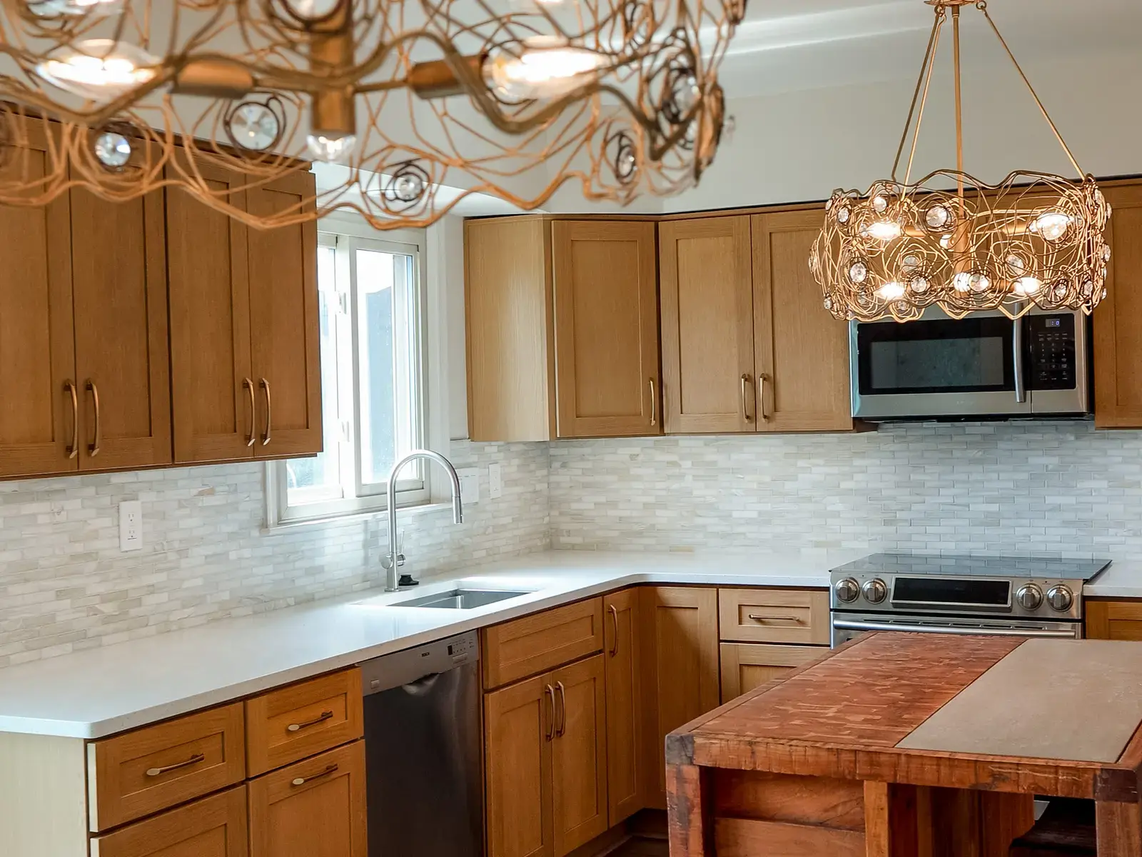 Finished kitchen with warm wood cabinetry, pale counters, and layered statement lighting
