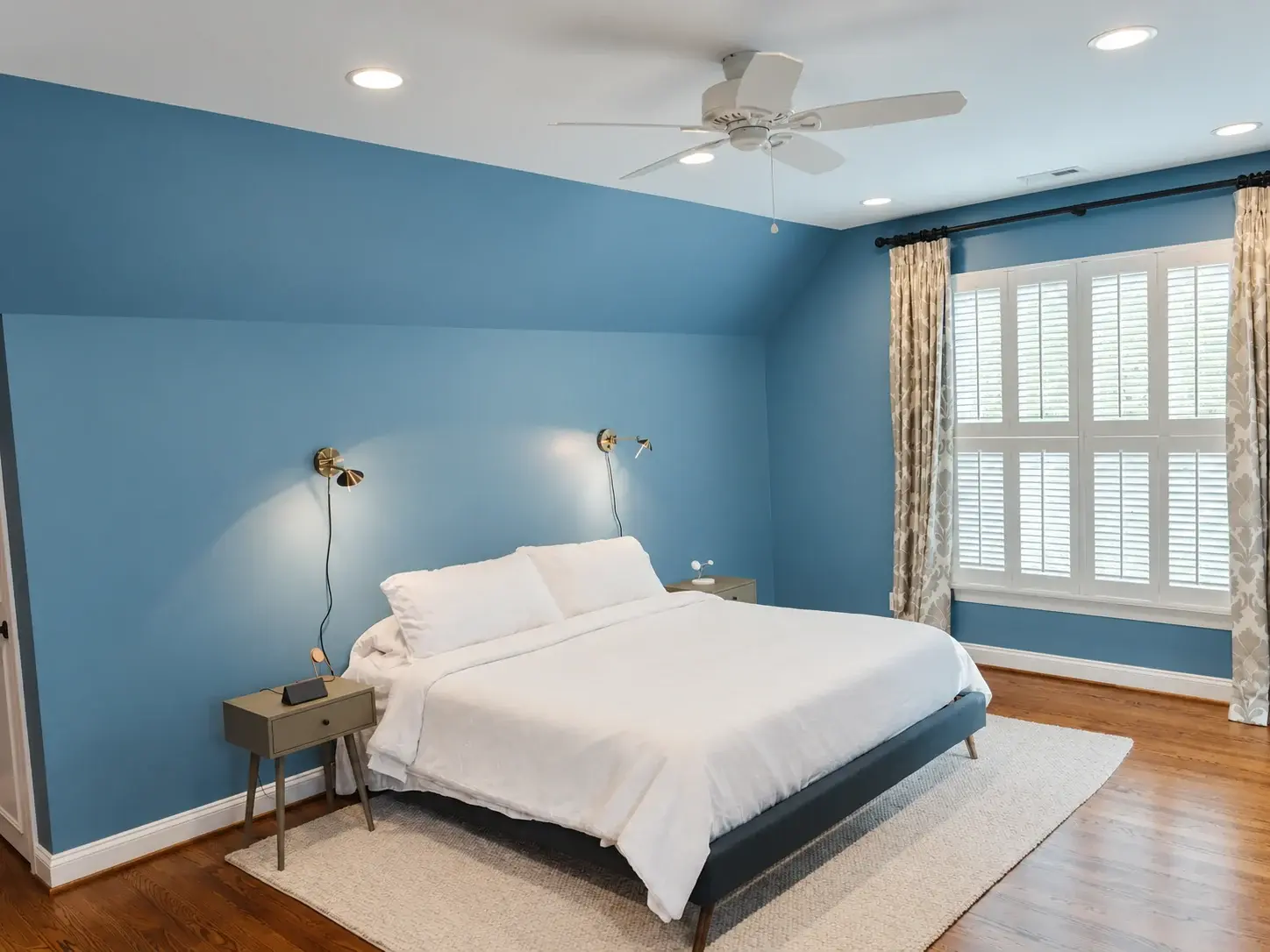 Blue bedroom with a finished dark plank floor visible around a large light area rug