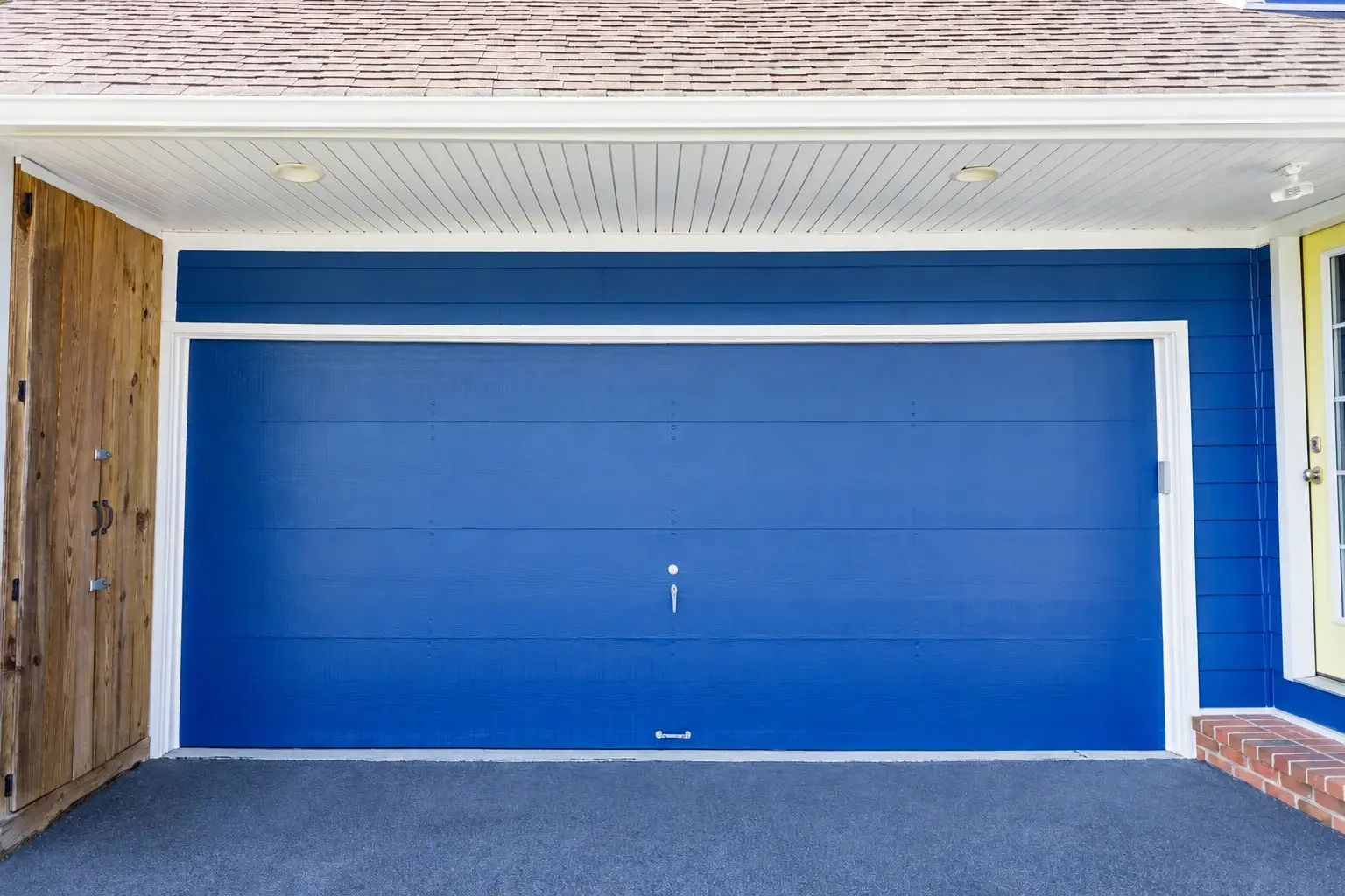 Blue garage door framed by white trim beneath a white porch ceiling