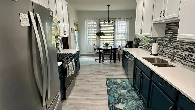 Galley kitchen with dark lower cabinets, white uppers, and patterned backsplash