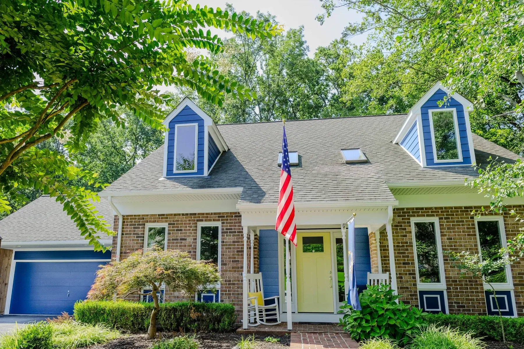 Finished cottage exterior with coordinated blue trim, garage door, dormers, and a warm front entry