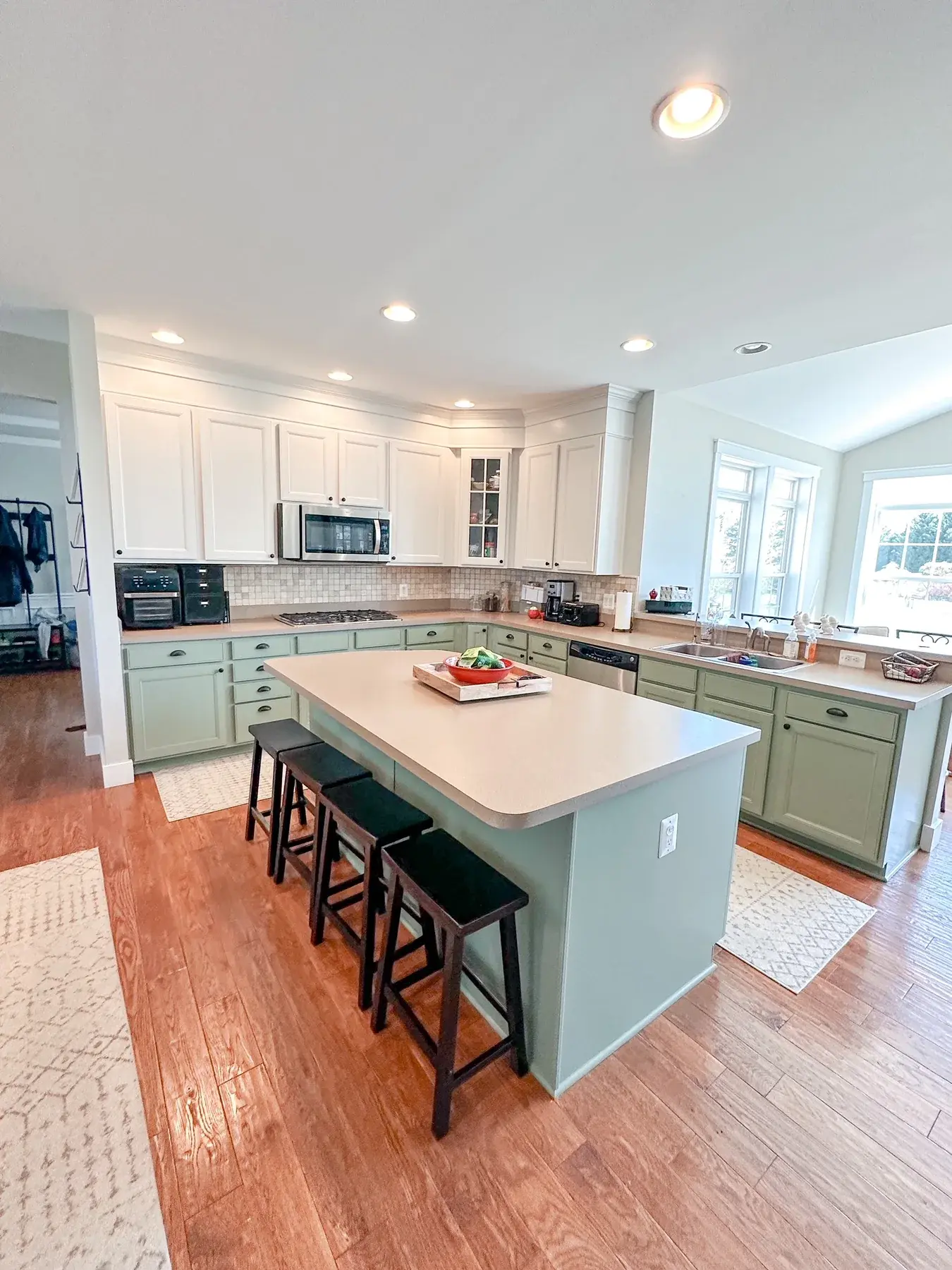 Finished kitchen with white upper cabinets, softly colored lower cabinetry and island, and warm wood flooring